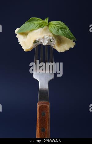 Köstliche Ravioli mit Käse und Basilikum auf Gabel vor dunkelblauem Hintergrund, Nahaufnahme Stockfoto