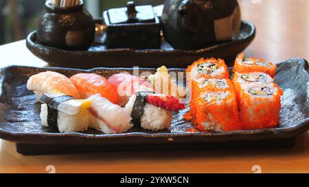 Verschiedene Sushi-Platte mit Nigiri und Rollen auf schwarzer Keramikplatte, Stockfoto
