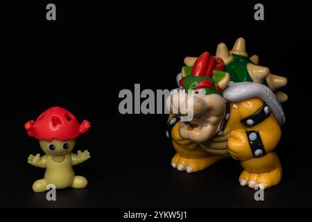 Zwei Plastikfiguren stehen auf schwarzem Hintergrund. Pilzähnliche Figur von Kinder Surprise mit King Bowser Figur von Super Mario. Stockfoto