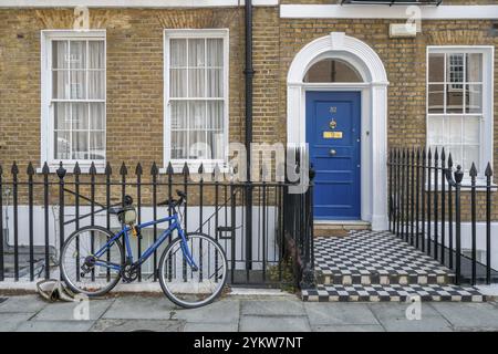 Ein blaues Fahrrad, das sich gegen einen schwarzen Zaun vor einer blau lackierten Haustür in einer klassischen britischen Ziegelfassade lehnt, Holborn, London Borough of CAMD Stockfoto