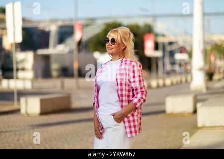 Frau in einem rosa karierten Hemd genießt einen sonnigen Tag auf einem stadtplatz Stockfoto