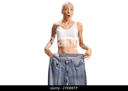 Schockierte junge Frau, die eine große Jeans auf weißem Hintergrund hält Stockfoto