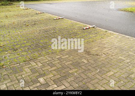 Leerer Parkplatz mit Moos zwischen den Pflastersteinen und einigen Verkehrsbarrieren Stockfoto