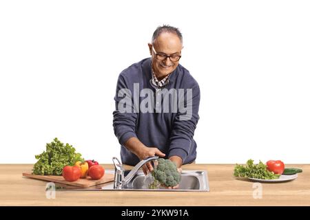 Mann, der Brokkoli und anderes Gemüse in einer Küchenspüle auf weißem Hintergrund wäscht Stockfoto