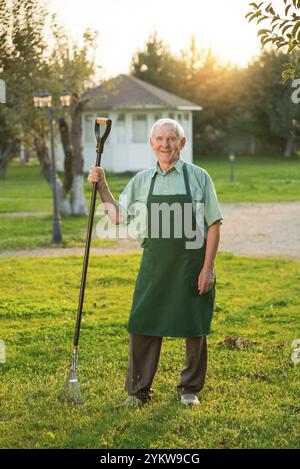 Senior Gärtner mit Rechen lächelnd. Alter Mann, der auf Gras steht. Beste Gartentipps Stockfoto