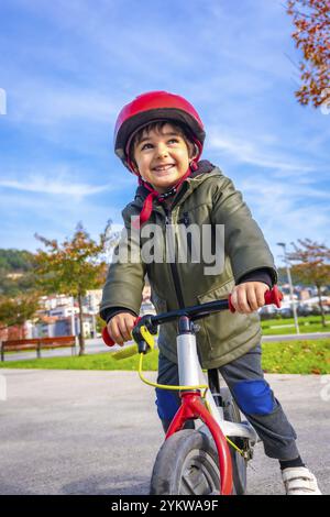 Ein kleiner Junge fährt mit einem roten Helm auf dem Fahrrad. Er lächelt und amüsiert sich Stockfoto