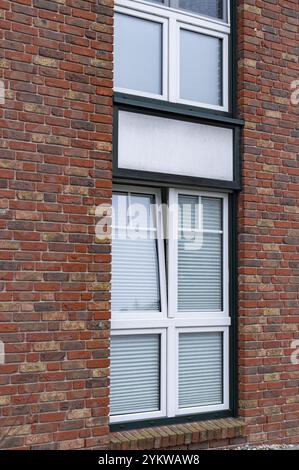 Geöffnetes Fenster mit abgesenkten venezianischen Jalousien an der roten Ziegelwand, die natürliches Licht im Inneren ermöglichen Stockfoto