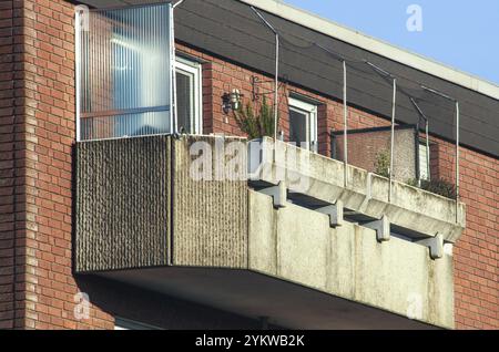Nahansicht eines Betonbalkons mit Plexiglasgehäuse und Vogelgeflecht, der an einem Backsteingebäude angeschlossen ist Stockfoto