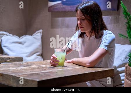 Eine Frau sitzt an einem Tisch mit einem Glas Limonade vor sich. Sie ist in kontemplativer Stimmung Stockfoto