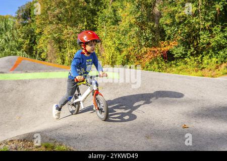 Ein kleiner Junge fährt Fahrrad auf einer Feldpiste. Er trägt ein blaues Hemd und einen roten Helm Stockfoto