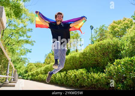 Ein Mann springt mit einer Regenbogenfahne in die Luft. Die Szene ist lebendig und fröhlich, und die Handlungen des Mannes vermitteln ein Gefühl der Freiheit Stockfoto