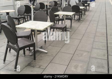 Nasse Rattanstühle und Tische stehen bei Regen auf einem grauen Pflaster eines leeren Cafés im Freien Stockfoto