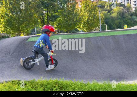 Ein kleiner Junge fährt mit dem Fahrrad einen Hügel hinunter. Der Junge trägt einen Helm und ein blaues Hemd. Die Szene ist draußen und der Junge genießt seine Fahrt Stockfoto