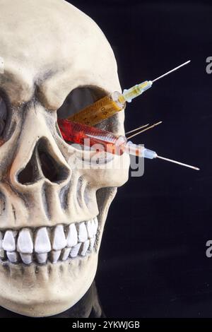 Menschenschädel mit bunten Spritzen im Augenloch. Isoliert auf schwarzem Hintergrund Stockfoto