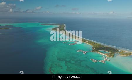 Atemberaubende Perspektive auf tropische Insel Korallenriffmotu, Überwasser-Bungalows in kristallklarer türkisfarbener Lagune, riesiger pazifik. Luxuriöses Urlaubsresort in wilder Natur. Drohnenaufnahme Stockfoto