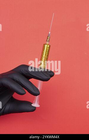 Handspritze gefüllt mit gelbem Glitzer. Vertikaler roter Hintergrund. Schwarzer Latexhandschuh Stockfoto