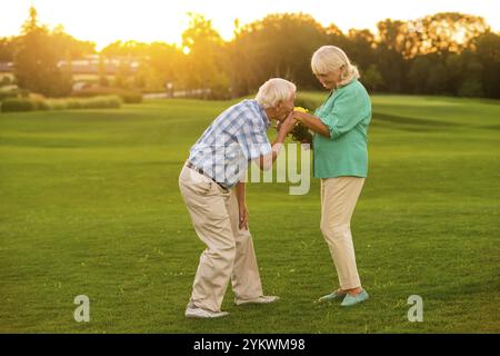 Ein älterer Mann, der die Hand der Frau küsst. Ein Paar, das auf einer Wiese steht. Liebevolles Herz des Gentleman. Unsere Gefühle sind stark Stockfoto