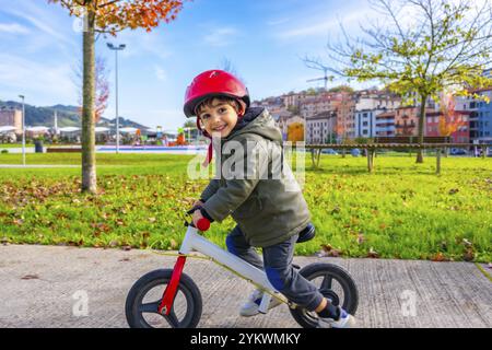 Ein kleiner Junge fährt mit Helm auf dem Fahrrad. Der Junge lächelt und er genießt sich. Die Szene spielt in einem Park, mit einer Bank und einer F Stockfoto