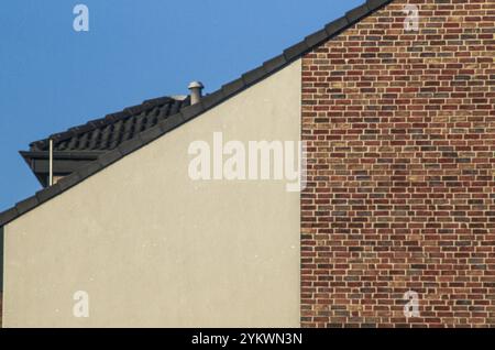 Architektonisches Detail mit kontrastierenden Texturen und Farben des modernen Häuseraußens mit verputzten und Ziegelwänden, Dachziegeln und Kamin gegen c Stockfoto