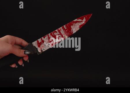 Die Nahaufnahme der weiblichen Hand hält ein mit Blut beflecktes Messer. Isoliert auf schwarzem Hintergrund Stockfoto