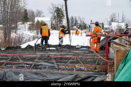 Arbeiter, die Beton mit einer Betonpumpe gießen, um eine Platte zu bauen, im Winter Stockfoto