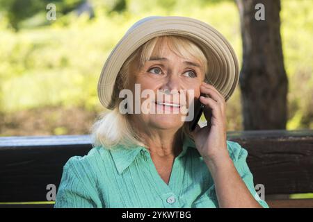 Senior Frau am Telefon. Reife Dame mit Hut. Bleiben Sie mit Verwandten in Kontakt. Billig ins Ausland telefonieren Stockfoto