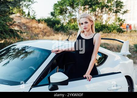 Fahrerin in schwarzem Kleid, die am Rennwagen steht Stockfoto