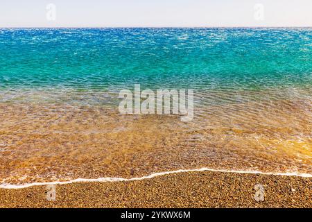 Klare Wellen der Ägäis, die am farbenfrohen Kieselstrand der Insel Kreta während des sonnigen Sommertages plätschern. Stockfoto