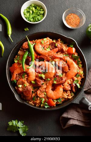 Kreolischer Jambalaya mit Garnelen, geräucherten Würstchen und Gemüse in gusseiserner Pfanne auf dunklem Hintergrund. Nahansicht Stockfoto