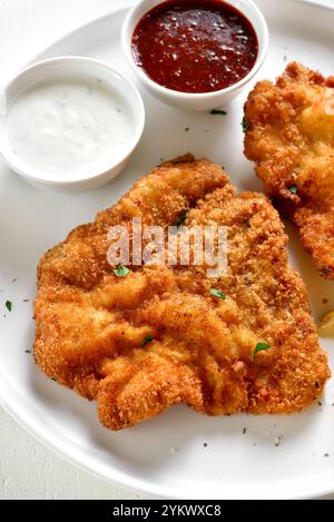 Paniertes wiener Schnitzel, serviert mit Sauce auf Teller auf weißem Hintergrund. Nahansicht Stockfoto