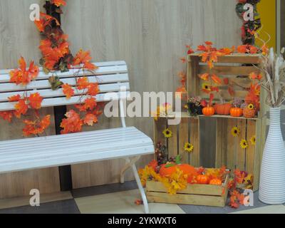 Gemütliche Herbstecke mit weißer Bank und orangefarbenen Blättern und Gemüse, festliche Dekoration zum Thema Herbst und Ernte mit künstlichem Laub Stockfoto