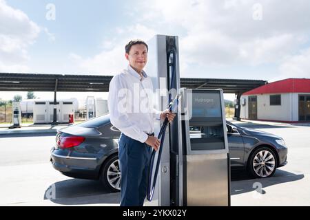 Der Mann hält eine Wasserstoffdüse an einer Wasserstofftankstelle. Auto mit Wasserstoff betanken. Stockfoto