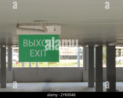 Grüne Informationstafel mit der Aufschrift Exit in englischer und russischer Sprache ​​hanging unter der Decke eines überdachten Parkplatzes Stockfoto