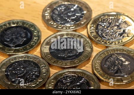 Nahaufnahme mehrerer 1-Pfund-Münzen, die auf einer hellbraunen Holzoberfläche verstreut sind. Die Münzen zeigen das Profil von Königin Elisabeth II. Und andere Entwürfe. Stockfoto