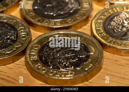 Nahaufnahme mehrerer britischer 1-Pfund-Münzen auf einer hellbraunen Holzoberfläche. Die Münzen stehen im Mittelpunkt und zeigen Details des Designs und der Inschrift Stockfoto