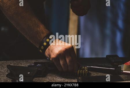 Mann mit Munition. Auf dem Tisch befindet sich eine Pistole in einem Holster, eine Reihe von Kugeln und ein Magazin oder Clip zum Laden des Stockfoto