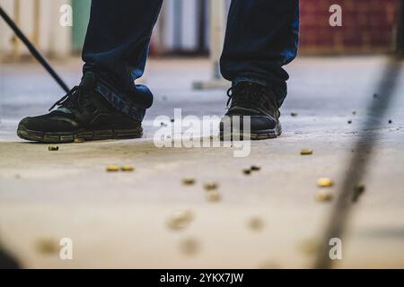 Nahaufnahme der Füße einer Person. Die Person trägt schwarze Schuhe und dunkle Hosen. Der Boden scheint mit einer verschwendeten Kugel bedeckt zu sein Stockfoto