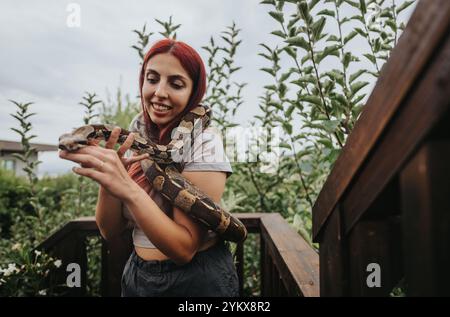 Lächelndes Mädchen, das eine große Schlange in einem üppigen Garten hält Stockfoto