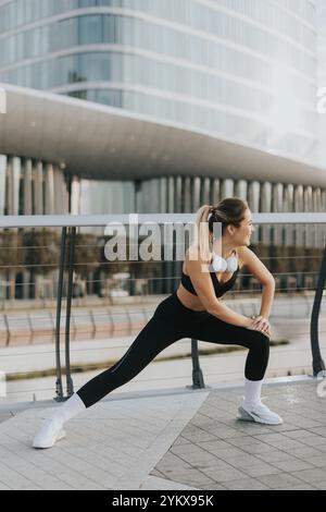 Eine Frau in eleganter Aktivkleidung macht sich im Freien stark und konzentriert sich auf ein belebendes Workout vor dem Hintergrund Stockfoto