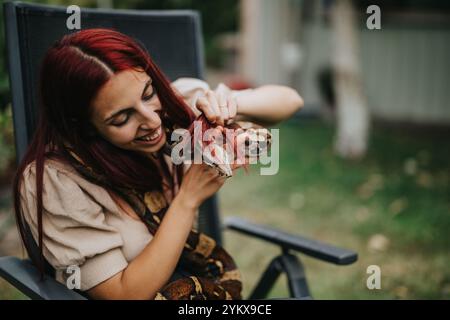 Mädchen mit roten Haaren lächelt, während sie draußen eine große Schlange hält Stockfoto
