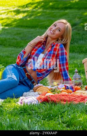 Ein atemberaubendes europäisches Model, gekleidet in gemütlichen Herbstschichten, genießt an einem frischen Herbsttag ein malerisches Picknick im Freien. Goldene Blätter umgeben sie während sie Stockfoto