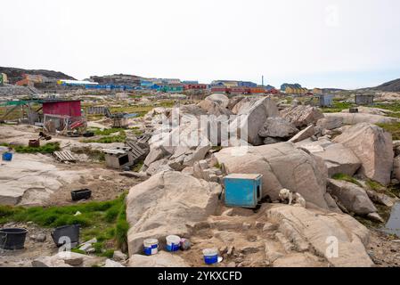 Grönländische Schlittenhunde in der Stadt Ilulissat im Hintergrund. Die farbenfrohen Häuser von Ilulissat bilden einen markanten Kontrast zu der weiten Gegend mit dem t Stockfoto