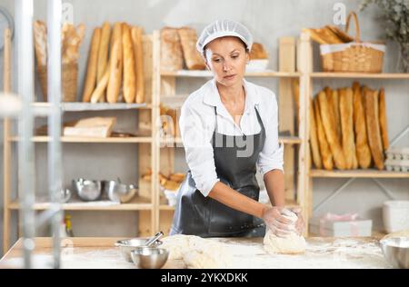 Bäckerin steht an seiner Werkbank und knete und formt Teig, um Brot, Croissants und Baguettes zu machen Stockfoto