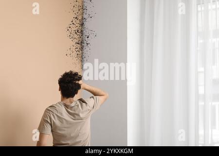 Verblüffter junger Mann, der auf Schimmel an der Wand seiner Wohnung blickt Stockfoto