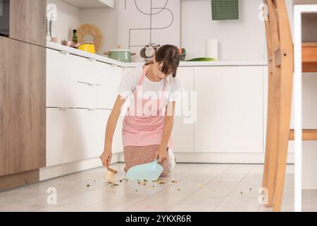 Junge Hausfrau, die in der Küche verstreutes Gemüse vom Boden fegt Stockfoto