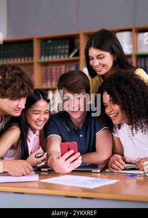 Verschiedene Gruppen von Schülern, die gemeinsam in der Bibliothek auf das Handy lächeln. Stockfoto