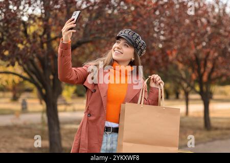 Weibliche Touristenin mit Einkaufstasche, die Selfie im Park am Herbsttag macht Stockfoto