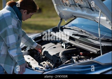 Kaukasische Fahrerin, die den Ölstand im Fahrzeugmotor überprüft. Stockfoto