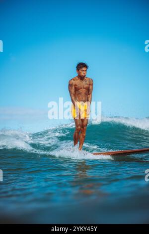 Ein Mann in gelben Shorts steht auf einem Surfbrett im Meer. Stockfoto