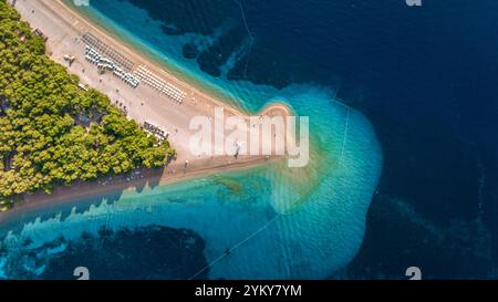 Goldener Sand erstreckt sich in der Dämmerung in das kristallklare türkisfarbene Wasser des Strandes Zlatni Rat auf Brac Island, wo Besucher die atemberaubende nat genießen Stockfoto